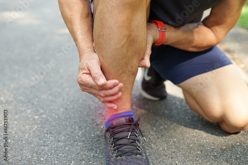 senile runner's hands supporting ankle in pain due to sprained ankle, selective focus