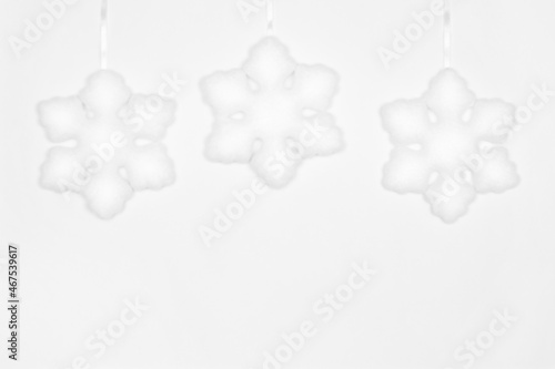 Three hanging white snowflake decorations on white wall. Copy space. Simple winter background