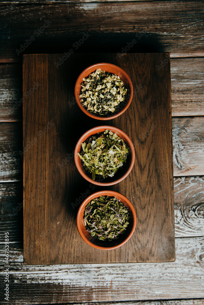 Assortment of dry tea in brown ceramic bowls on a wooden board, in a rustic kitchen Assortment of dry tea in brown ceramic bowls on a wooden board, in a rustic kitchen