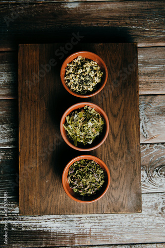 Assortment of dry tea in brown ceramic bowls on a wooden board, in a rustic kitchen