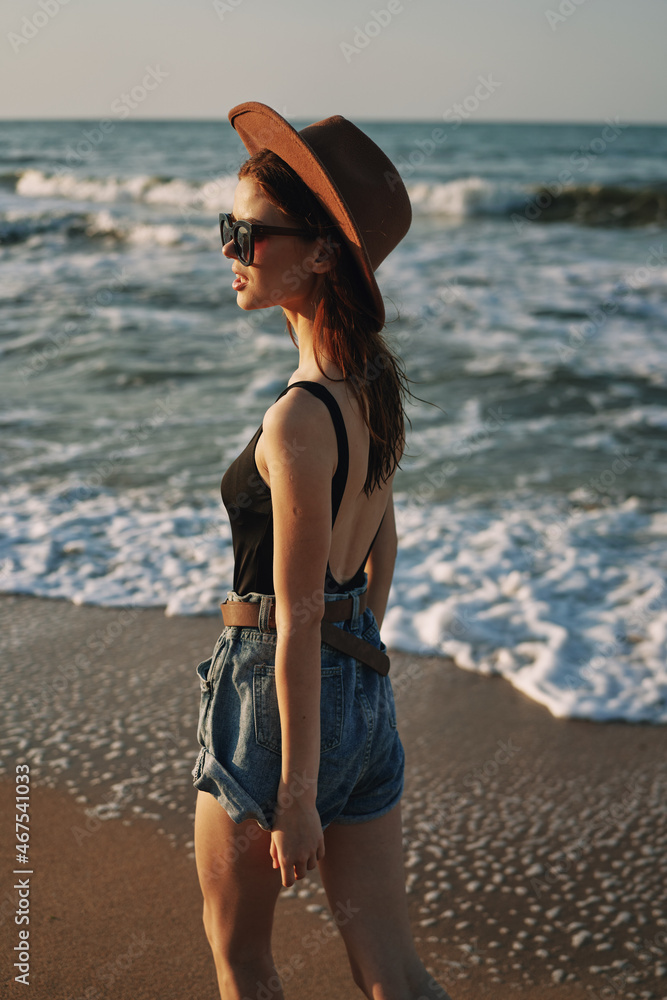 cheerful woman in sunglasses and a hat walks along the ocean