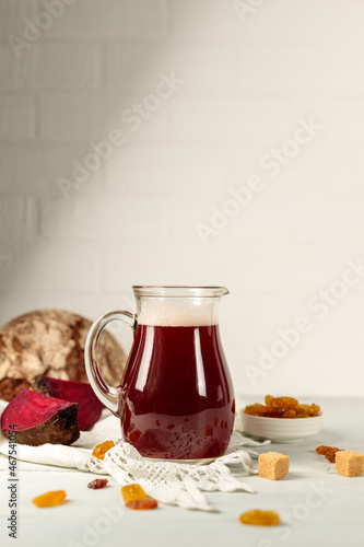 A jug of homemade fermented drinks. Beet kvass on a linen napkin, with ingredients for cooking. Vertical, natural light