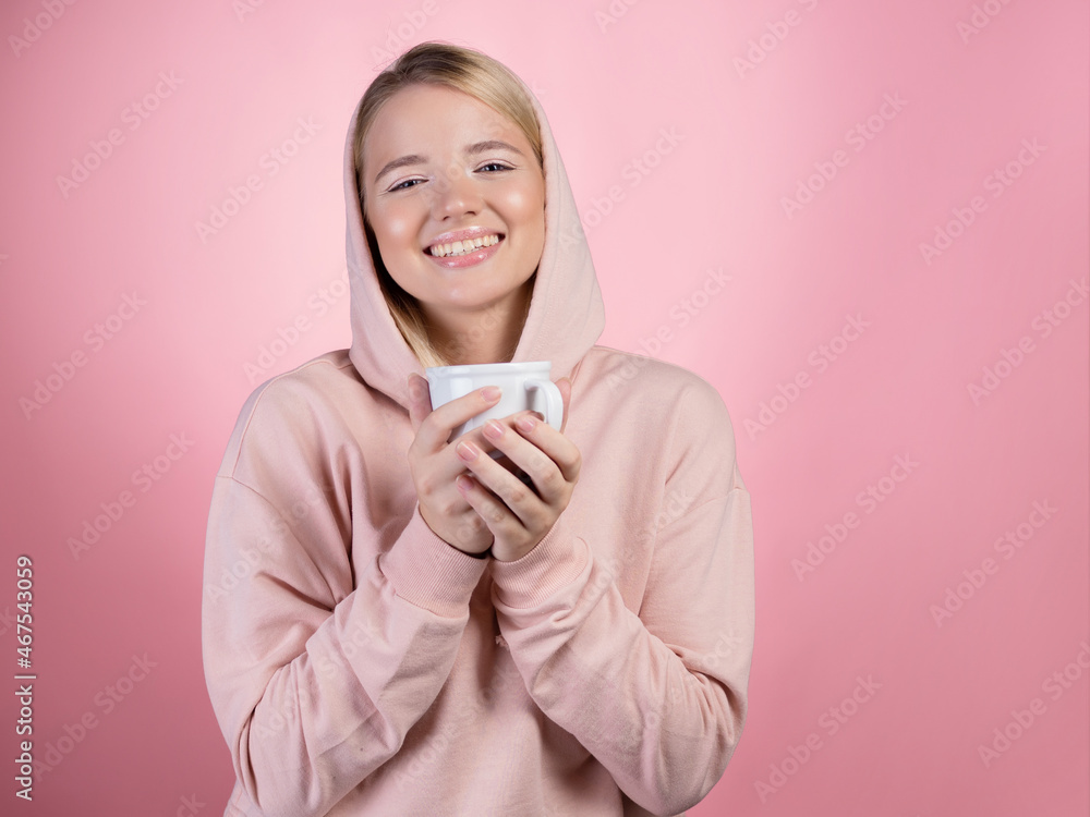 Drink a hot drink, keep warm in cold weather. A young woman with a hood on her head drinks a hot seasonal drink, tea, coffee or mulled wine Drink a hot drink, keep warm in cold weather. A young woman with a hood on her head drinks a hot seasonal drink, tea, coffee or mulled wine