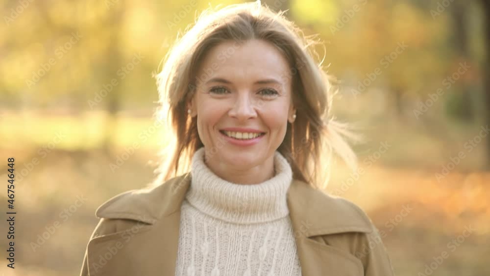 Smiling Gorgeous Woman looking into the camera against trees at park during autumn. Attractive lady is walking on the alley full of trees Smiling Gorgeous Woman looking into the camera against trees at park during autumn. Attractive lady is walking on the alley full of trees