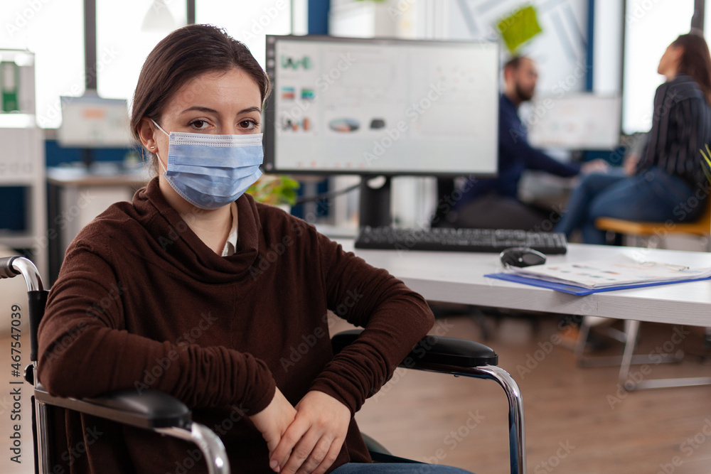 Portrait of disabled businesswoman with medical face mask against covid19 working in startup business office. Executive manager in wheelchair planning management strategy