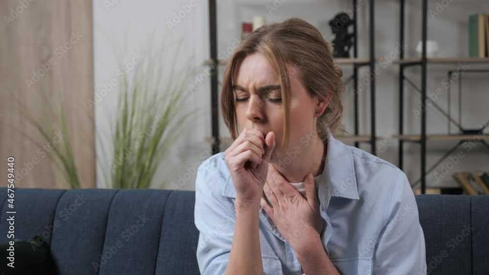 Sick girl dressed in casual clothes coughs during covid pandemic 19 at home. Inflammation of the respiratory tract, virus, infection. Woman coughs into a medical mask and feels bad indoor. Sick girl dressed in casual clothes coughs during covid pandemic 19 at home. Inflammation of the respiratory tract, virus, infection. Woman coughs into a medical mask and feels bad indoor.