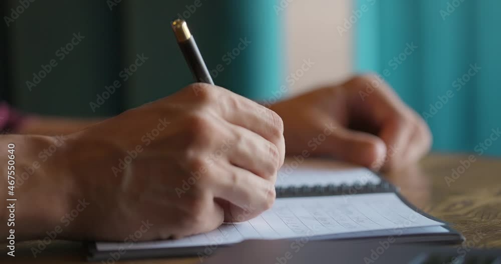 Male hands writing in paper notebook while sitting at wooden table next to the window Male hands writing in paper notebook while sitting at wooden table next to the window
