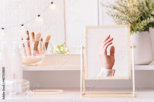 Reflection in table mirror of woman hand.   hristmas  light bulbs  eucalyptus  fir   pine branches in a vase  on dressing table with make up accessories.