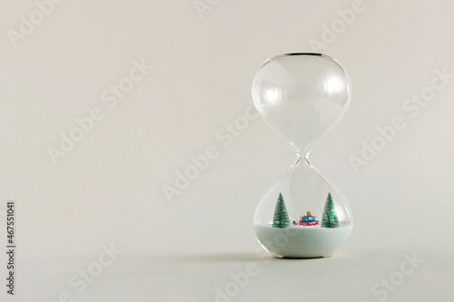 2022. Fir christmas trees and Santa’s sleigh with presents, standing in the hourglass isolated on pastel beige background. Evergreen nature winter New Year idea. Minimal Xmas greeting card concept.