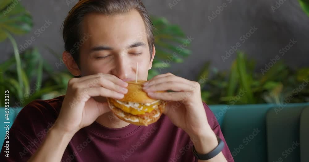 Close up of young handsome brunet eating burger in nice coffee shop.Man enjoying meal Close up of young handsome brunet eating burger in nice coffee shop.Man enjoying meal
