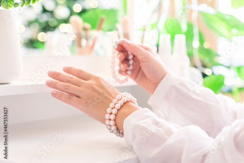 Woman puts on jewelry  pearl bracelets on the hand and  sitting near dressing table with make up accessories.