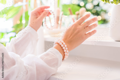 Woman puts on jewelry, pearl bracelets on the hand and  sitting near dressing table with make up accessories.
