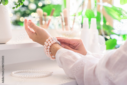 Woman puts on jewelry, pearl bracelets on the hand and sitting near dressing table with make up accessories.