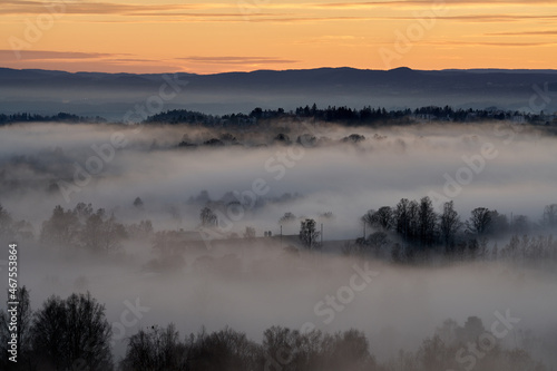 The fog is dense but the sun is cracking out. Shot in the evening from a height over Oslo city in Norway. The fog is like a blanket over the people and city.  Shot in autumn. 