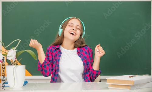 happy teen girl hold modern headphones in high school at blackboard, childhood © Olena