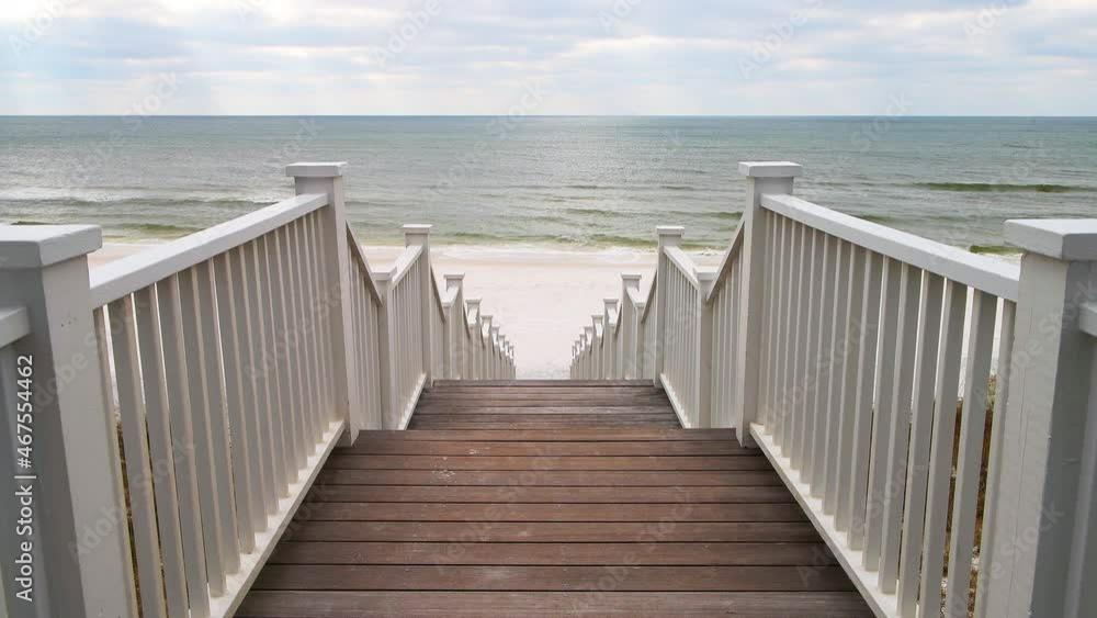 High angle aerial view through wooden pavilion boardwalk white railing stairs steps by beach at Gulf of Mexico at Seaside, Florida with people on coast shore High angle aerial view through wooden pavilion boardwalk white railing stairs steps by beach at Gulf of Mexico at Seaside, Florida with people on coast shore
