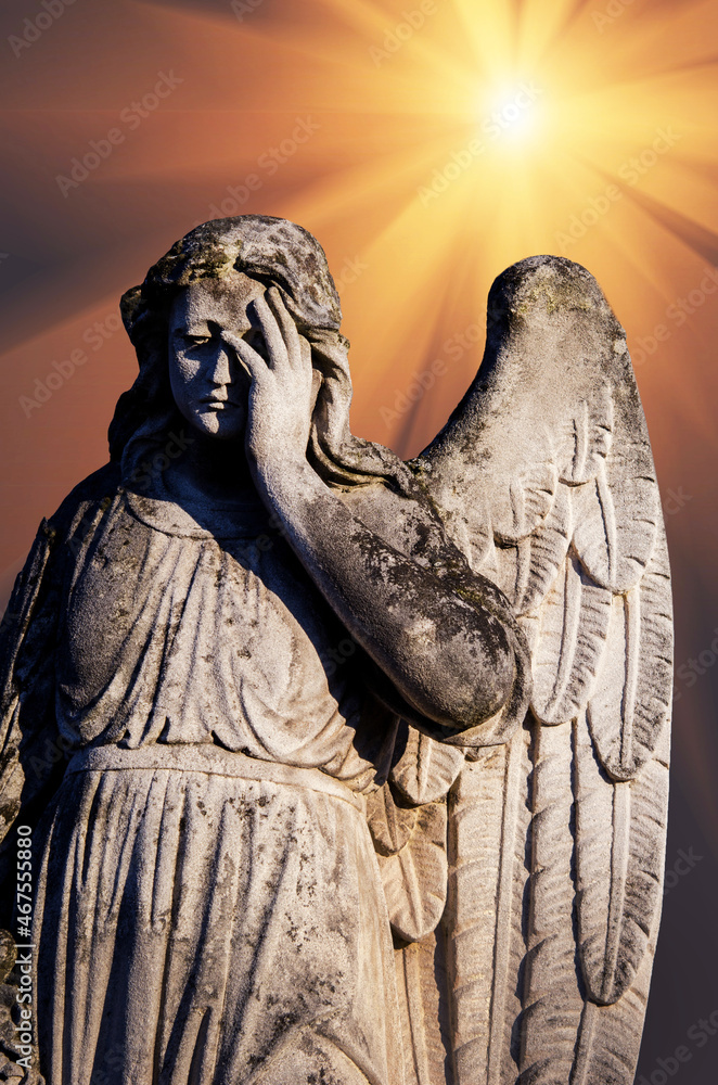 An ancient sculpture of a sad angel mourning the dead, against the background of rays of light that symbolize hope.