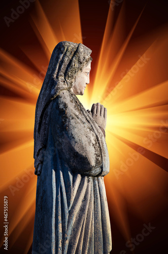 An ancient sculpture of the Virgin Mary with folded hands in prayer against the background of rays of light, which symbolize the personification of the Holy Spirit.