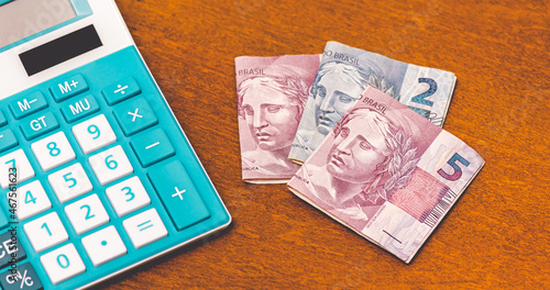 Dinheiro, Brasil. Cédulas do Real Brasileiro - BRL, sobre uma mesa de madeira com uma calculadora azul. Aumento da Inflação na economia brasileira. photo