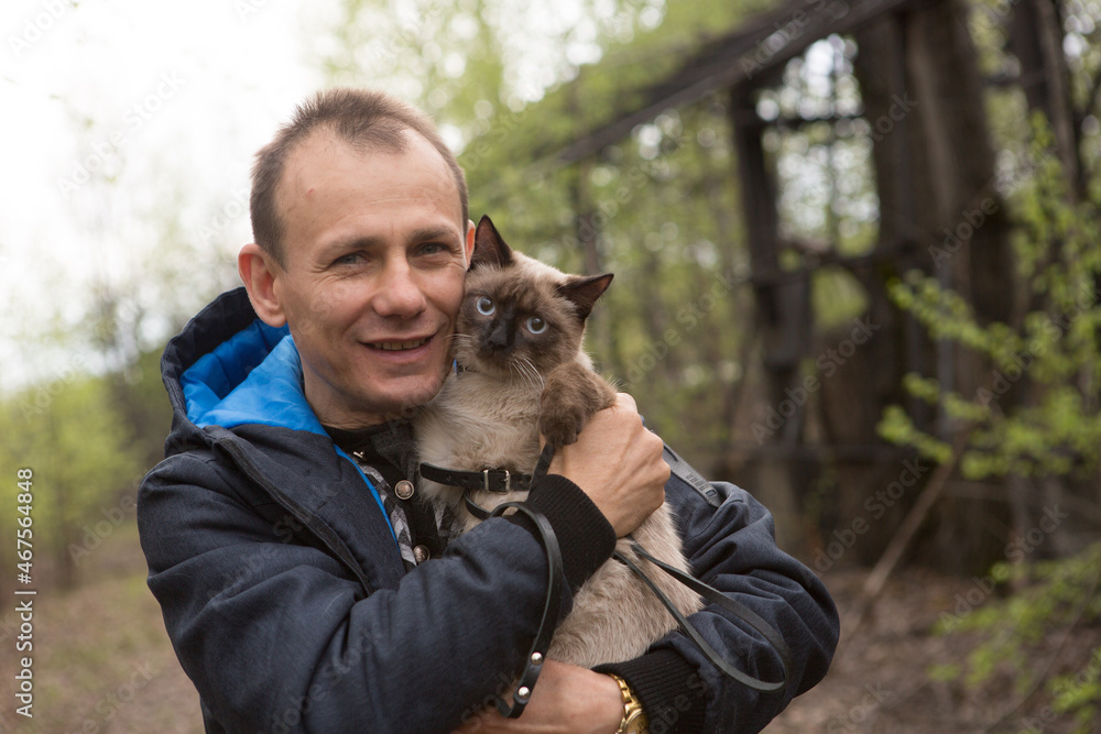 A caring man holds a cat in his arms, both look into the camera A caring man holds a cat in his arms, both look into the camera