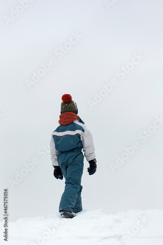 Back view the child walks in the winter on the street. Boy walks on loose snow. Cold winter day. Vertical frame