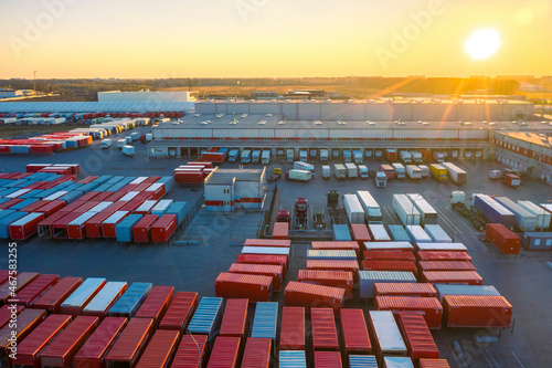 Aerial view of a logistics park with warehouse, loading hub and many semi trucks with cargo trailers standing at the ramps for load/unload goods at sunset. 