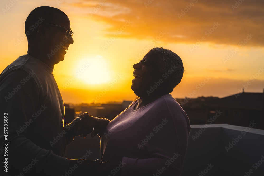 Happy Latin senior couple having romantic moment dancing on rooftop during sunset time
