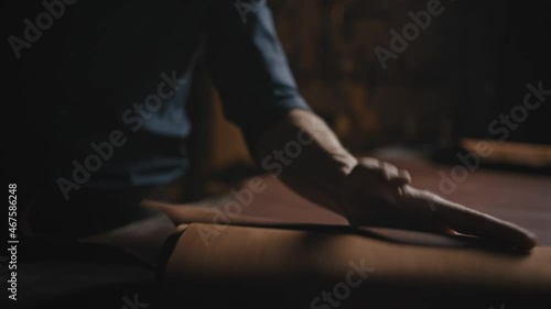 Shoes production. Unrecognizable man shoe maker rolling out piece of leather for cutting needed amount at workshop photo