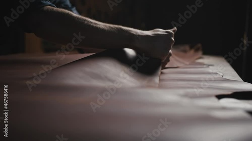 Unrecognizable man tailor smoothing out leather on table, examining fabric quality before work with it, close up photo