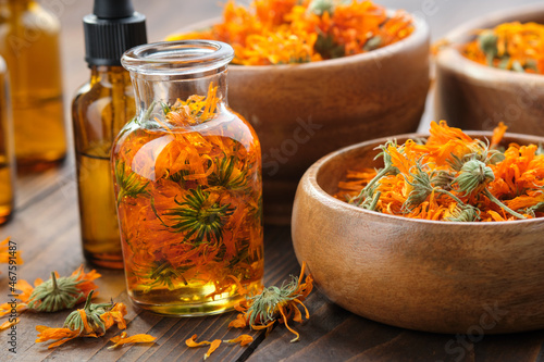 Bottles of calendula essential oil or infusion, wooden bowls and mortar of dried healthy calendula marigold flowers. Alternative herbal medicine. Aromatherapy.