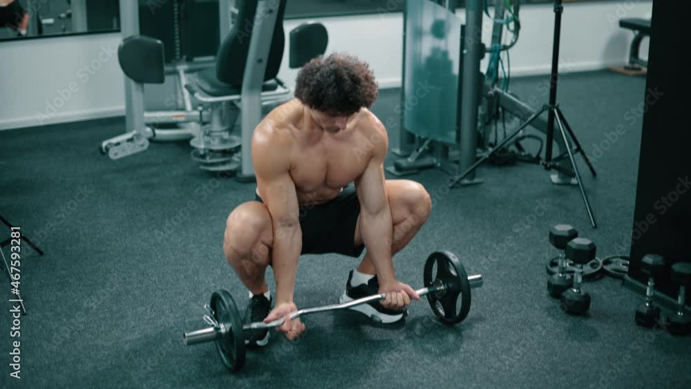 Athlete takes barbell from floor and trains biceps in gym. Athlete takes barbell from floor and trains biceps in gym.