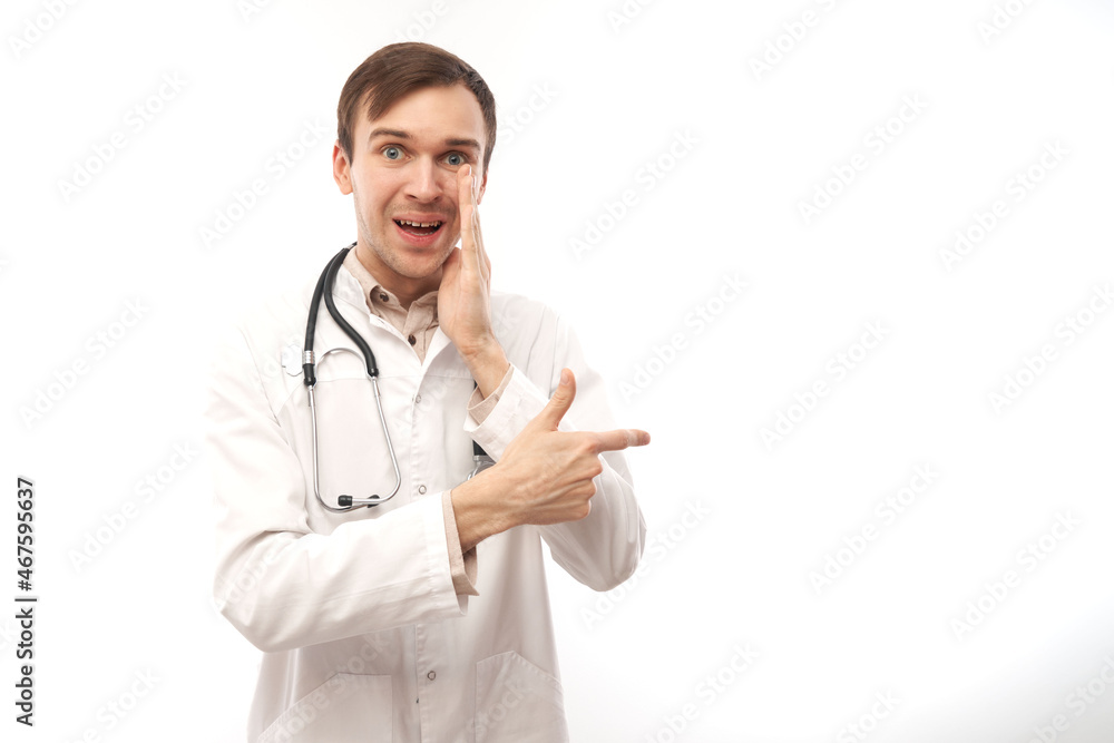 Handsome doctor in white medical coat with stethoscope points finger at empty space isolated on white background with copy space. Demonstrates product, excitedly shows something Handsome doctor in white medical coat with stethoscope points finger at empty space isolated on white background with copy space. Demonstrates product, excitedly shows something