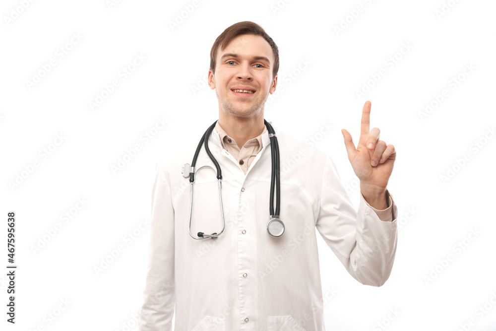 Handsome doctor in white medical coat with stethoscope points finger at empty space isolated on white background with copy space. Demonstrates product, excitedly shows something Handsome doctor in white medical coat with stethoscope points finger at empty space isolated on white background with copy space. Demonstrates product, excitedly shows something