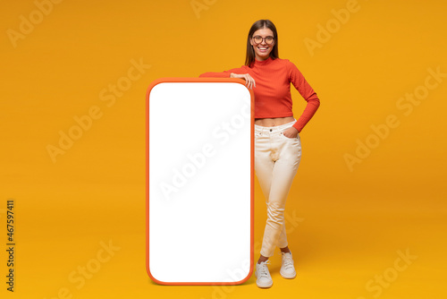 Happy young woman standing and showing blank screen of huge phone, mockup for your app photo