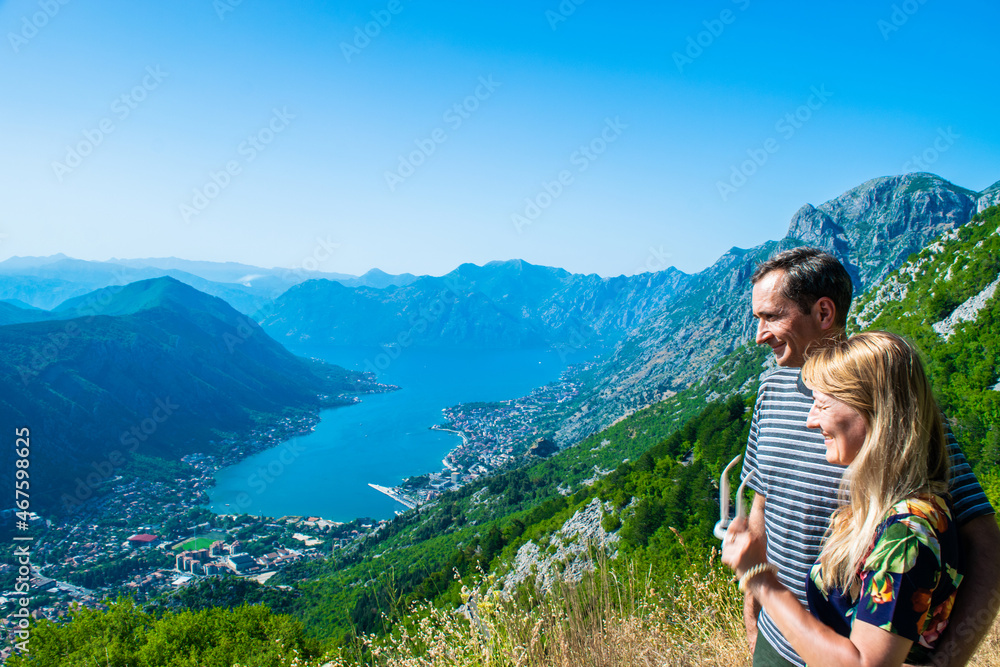 Naklejka premium Couple man and woman tourists on Boka Kotorska Bay and coastal towns at foot of mountain ranges. Summer blue landscape. Adriatic Sea. Montenegro.