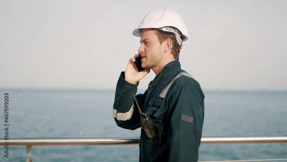 Young happy port worker talking with family on mobile phone and smiling while walking in seaport Young happy port worker talking with family on mobile phone and smiling while walking in seaport