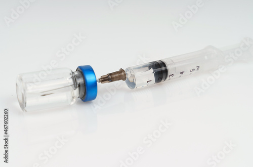 A syringe and a jar of injection lie on a white reflective surface.