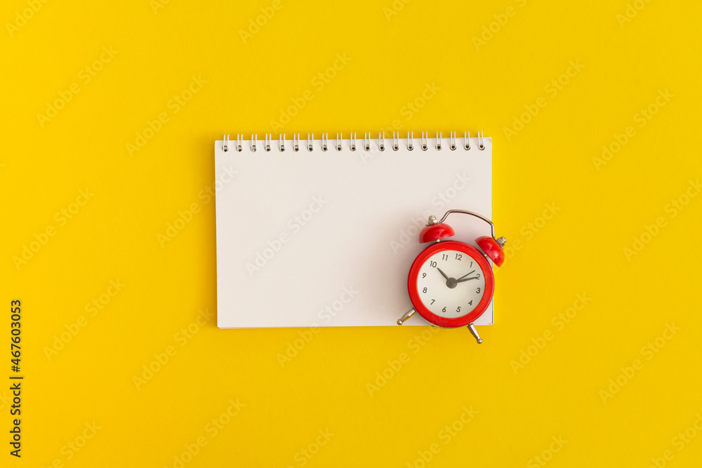 Red alarm clock and notebook with space for text on yellow background Red alarm clock and notebook with space for text on yellow background