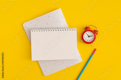 Red alarm clock and notebooks with space for text on yellow background