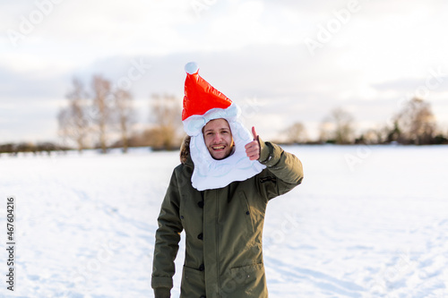A 20 something year old man wearing a funny inflatable Santa hat while outside in a snowy landscape