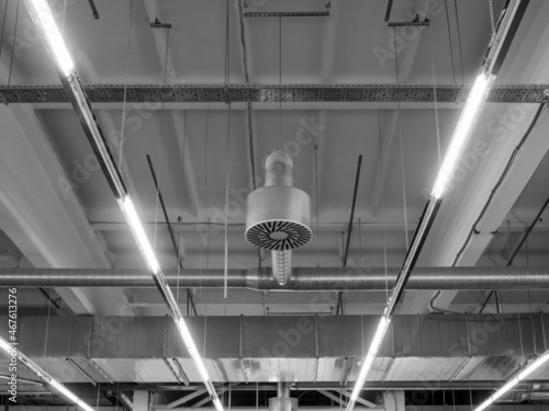 Ventilation and air conditioning system in industrial or commercial premises with lighting, under the ceiling. Ventilation pipes and hoods. Monochrome, symmetry, black and white image.