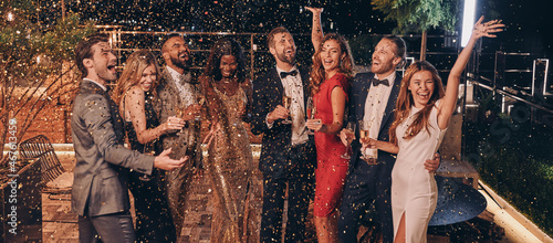 Foto Group of happy people in formalwear having fun together with confetti flying all