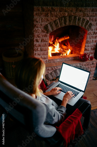 Cozy home. Pretty young woman working on laptop computer near the fireplace. Copy space on the screen.