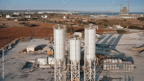 Cement concrete silo production factory. Huge industrial storage reservoir towers. Constructions development manufacturing site. Aerial dtone flight over factory equipment. Sea coast in background photo