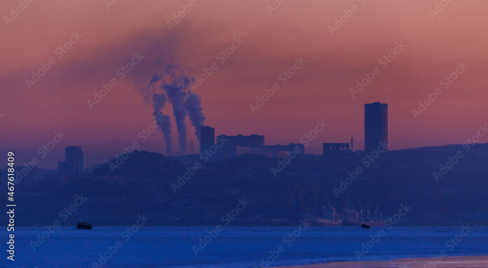 Early sunrise in Vladivostok city view from the sea. Smoke comes from chimneys against the background of residential buildings.