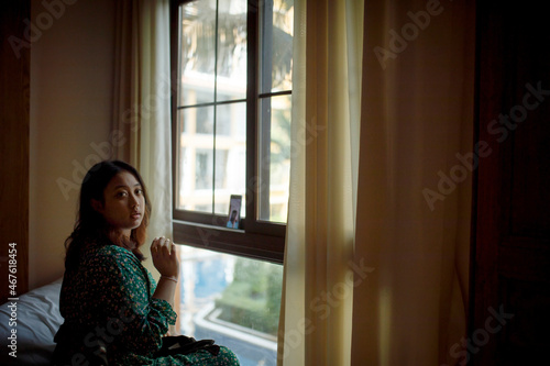 asian woman sitting beside window wih smartphone video call turn on