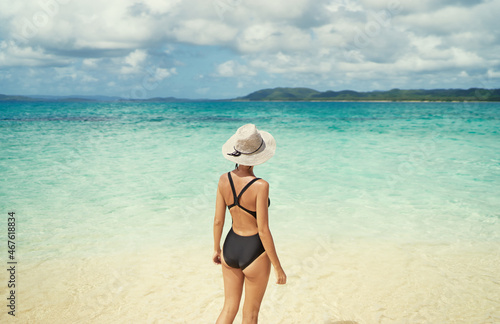 Vacation on the seashore. Back view of young woman walking away on the beautiful tropical white sand beach. © luengo_ua