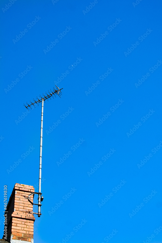 A TV antenna attached to a chimney with a bright blue sky as a backdrop. Image has copy space. A TV antenna attached to a chimney with a bright blue sky as a backdrop. Image has copy space.