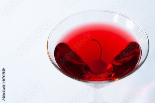 An isolated image of a martini glass with red liquid and a cherry inside on a white background. Image contains copy space.