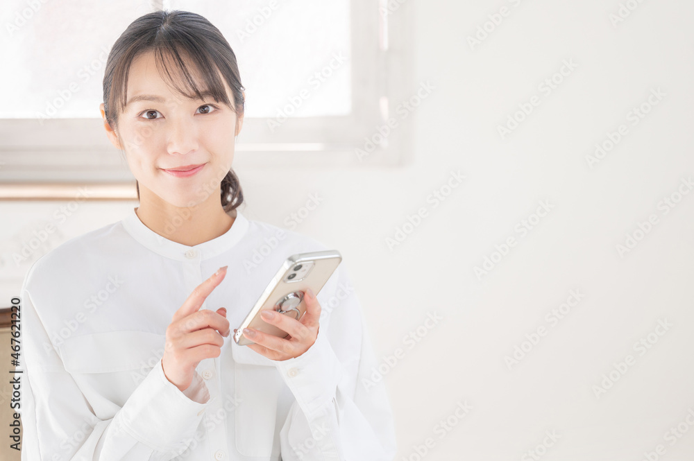 スマホでタップする美しいアジア人(日本人)女性のズーム 右にコピースペースあり カメラ目線 スマホでタップする美しいアジア人(日本人)女性のズーム 右にコピースペースあり カメラ目線